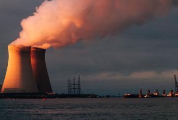 A power plant on a sea shore with smoke emerging from the towers. 